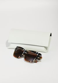 Gafas de sol con un audaz marco cuadrado en negro y patrones de carey, acompañadas de una funda rígida blanca marcada con "Burberry."