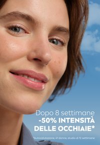 Primo piano di un volto con pelle liscia, trucco leggero e capelli castani corti e mossi, su uno sfondo blu tenue; testo riguardante la riduzione delle occhiaie.