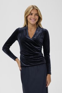 Top avvolgente in velluto blu navy con maniche lunghe, caratterizzato da una profonda scollatura a V e texture arricciata in vita, abbinato a una gonna scura.