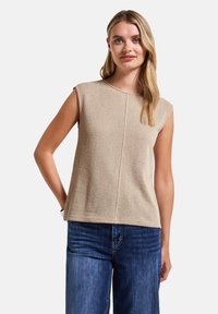 Top beige senza maniche con una finitura texturizzata, scollatura rotonda e taglio dritto. Abbinato a jeans in denim blu.