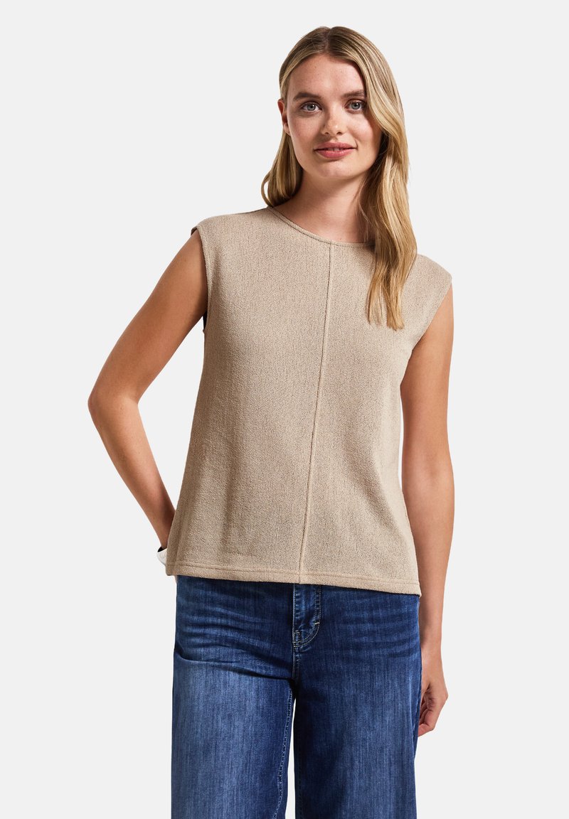 Top beige senza maniche con una finitura texturizzata, scollatura rotonda e taglio dritto. Abbinato a jeans in denim blu.