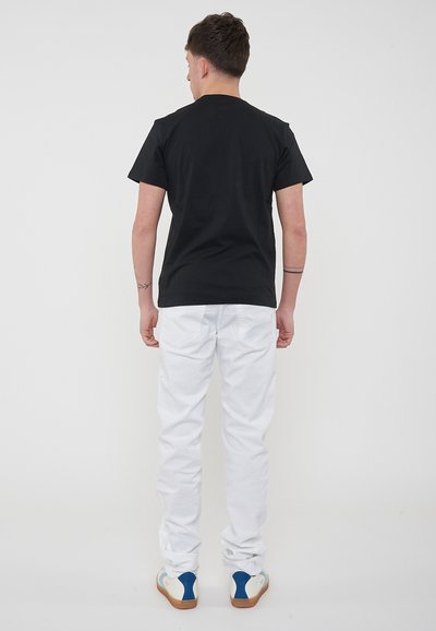 T-shirt in cotone nero, maniche corte, abbinato a jeans bianchi. Le scarpe hanno una base color crema e un accento blu sul tallone. Vista da dietro.