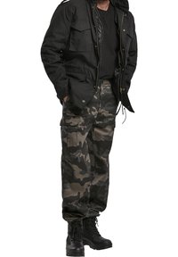 Svart zip-up jacka med flera framfickor, tillsammans medbyxor i kamouflagemönster och svarta snörade kängor.