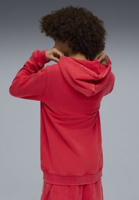 Roter Kapuzenpullover aus weicher Baumwolle, mit lockerer Passform und gerippten Bündchen. Die Kapuze und der Rücken sind sichtbar, mit einer glatten Textur.