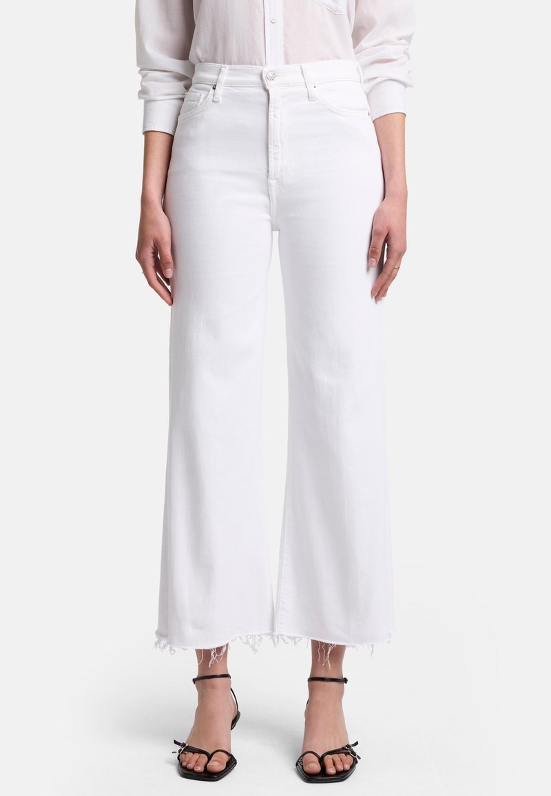 Jeans bianchi a vita alta con un taglio a gamba larga e orlo sfilacciato; realizzati in denim con una texture liscia. Abbinati a sandali neri con cinturini.