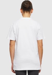 T-shirt en coton blanc avec un col rond, des manches courtes et une coupe décontractée. Dos uni sans logos ni motifs visibles.