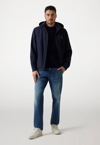 Giubbotto cappuccio blu navy con zip frontale, abbinato a una maglietta crewneck blu navy e jeans dritti azzurri. Sneakers bianche completano il look.