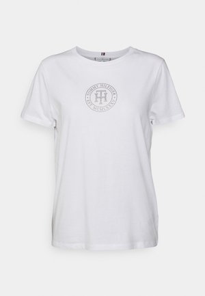 Biały t-shirt z krótkim rękawem i okrągłym dekoltem, z okrągłym logo Tommy Hilfiger i tekstem nadrukowanym na szaro na środku klatki piersiowej.