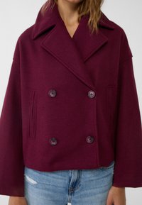 Burgundzka marynarka dwurzędowa z dużymi klapami, dwoma guzikami i bocznymi kieszeniami. Wykonana z miękkiego, teksturowanego materiału. Krótka długość.