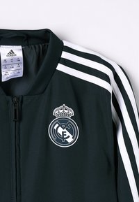 Sort Adidas jakke med hvide striber på skulderne og Real Madrid-logo på venstre bryst, størrelse XS til børn 7-8 år.