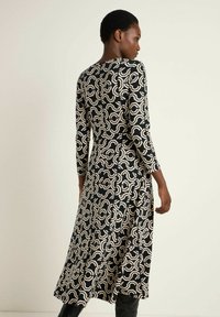 Langärmliges Kleid in Schwarz mit cremefarbenem abstraktem Muster, das eine fließende Silhouette und Textur aufweist, ergänzt durch einen runden Halsausschnitt.