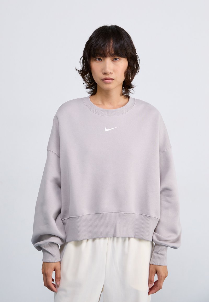 Ljusgrå sweatshirt med rund halsringning, ribbade ärmslut och nederkant, och en liten vit Nike-logotyp på bröstet. Mjuk tyg, oversize passform.