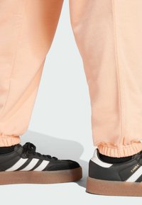 Čierne a biele tenisky s gumovými podrážkami, v kombinácii s broskyňovými teplákmi s elastickými manžetami a textúrovanou látkou.