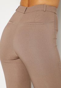 Pantalon beige ajusté avec une texture lisse, taille mi-haute et deux poches arrière. Design sur mesure avec des coutures discrètes.