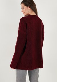 Burgundy knit sweater with a textured, fuzzy surface; relaxed fit, long sleeves, and a crew neckline.  Features ribbed detailing at cuffs.