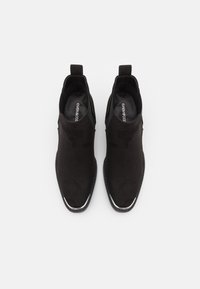 Mustat mokkanahka nilkkurit, joissa on joustavat sivupaneelit ja kiiltävä hopeinen yksityiskohta varpaan kohdalla. Sujuva pinta, tyylikäs muotoilu ja terävä muoto.