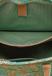 Turquoise tas met bloemenpatroon aan de binnenkant, met groene en donkergroene verticale gestreepte stofvoering en bruin leren rand en tab.