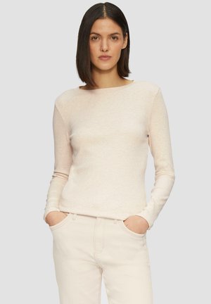 Lichtroze langemouwen top met een boothals. Zachte, gestructureerde stof. Het model draagt een lichte broek met zakken, handen rustend erin.