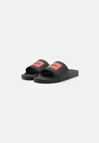 Svarte sandaler med glatt overflate, med bred reim som har en rød rektangulær logo. Teksturert såle for godt grep, minimalistisk design.