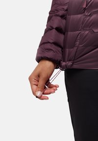Giacca a vento viola con design trapuntato e polsini elasticizzati. Un cordino regolabile tirato a mano all'orlo, che rivela una texture di tessuto liscia.