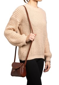 Maglione beige lavorato a maglia con un design morbido e texturizzato, abbinato a una piccola borsa a tracolla in pelle marrone con una patta curva e una tracolla.