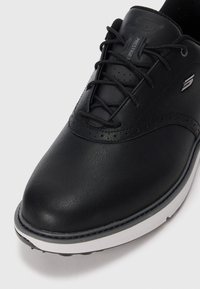 Sneaker en cuir noir à lacets avec semelle blanche et finition perforée subtile, arborant une étiquette "Prestige" sur la languette.