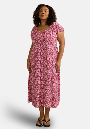 Maxi-jurk in roze met bloemenpatroon, korte pofmouwen, elastische taille en een ronde halslijn; gecombineerd met zwarte teenslippers.