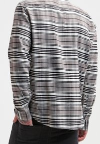Camicia a quadri grigia con bottoni, caratterizzata da linee nere e bianche, realizzata in cotone, maniche lunghe e orlo arrotondato.