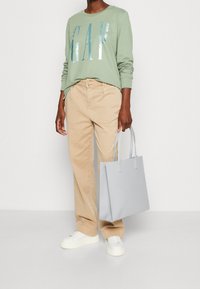Felpa verde chiaro con stampa di lettere argento, pantaloni beige, sneakers bianche e una borsa a tracolla grigia chiaro con logo a rilievo.