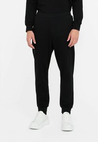 Sorte joggingbukser med elastisk liv, tapered ben og sidelommer, parret med hvide sneakers. Blød stofftekstur.