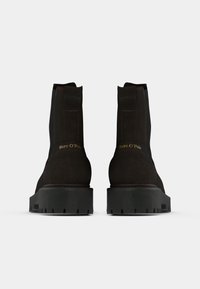 Bottines en suede marron avec une semelle en caoutchouc noir, dotées d'un bout arrondi et de languettes sur les côtés. "Marc O'Polo" embossé à l'arrière.