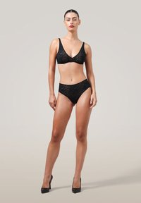 Svart spets-bh och högmidjade trosor set. Har ett blommönster, slät textur och tunna remmar. Bärs med svarta högklackade skor.