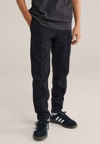 Svarta sportbyxor av mjukt tyg med tajt passform, synliga sömmar, sidfickor och slät yta. Kombinerade med mörka sneakers.