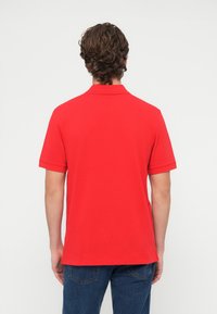 Czerwona koszulka polo z klasycznym kołnierzykiem i krótkimi rękawami, wykonana z gładkiego materiału, z kontrastowymi obszyciami na rękawach i kołnierzu.
