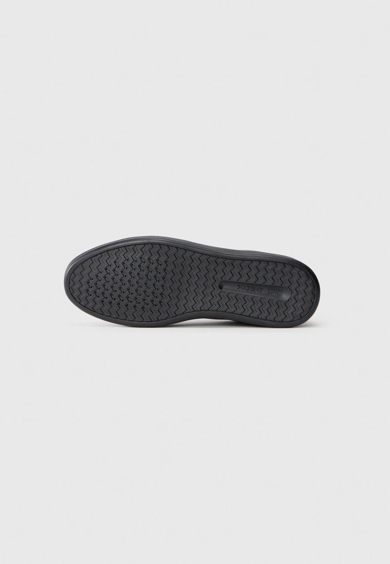 Suela de zapato de goma negra con un patrón de tracción en zigzag, bordes suaves y un detalle del logo ligeramente elevado en el centro.