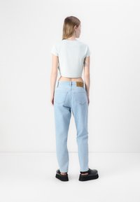 Vaaleansininen lyhyt croppitoppi, rento istuvuus denim-farkut ja mustat korokkenilkkurit. Ominaisuuksiin kuuluu takataskut ja merkkipatch vyötäröllä.