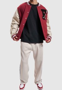 Veste universitaire rouge et crème avec boutons-pression, poignets côtelés et logo F. T-shirt noir et pantalon beige slim avec bandes latérales. Baskets rouges.