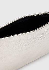 Zilveren leren clutch met een gestructureerd oppervlak, voorzien van een donkere stofvoering en een metalen rits langs de bovenrand.