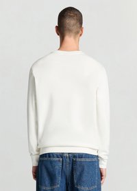 Sweatshirt blanc à col rond et manches longues, fabriqué en tissu lisse. Présente des poignets et un ourlet côtelés, associé à un jean en denim bleu.