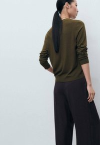 Olive green sweater with long sleeves and ribbed cuffs, paired with dark wide-leg trousers. Smooth texture with a simple design.