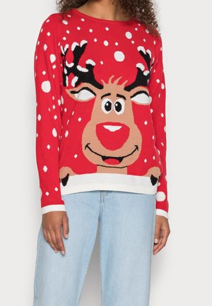 Pull rouge avec un grand visage de renne souriant et des motifs de flocons de neige blancs, porté avec un jean bleu clair.