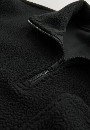 Sudadera de forro polar negra con un alto cuello, media cremallera con cremallera negra y tejido suave al tacto. Parte inferior lisa sin logotipos visibles.