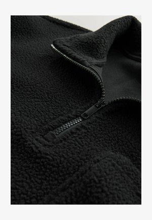 Pullover in pile nero con colletto alto, zip a metà con cerniera nera e tessuto morbido. Sottostrato liscio senza loghi visibili.