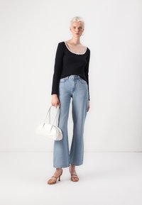 Svart langermet topp med hvit hals, tettsittende over liv. Lyseblå, vide jeans, lyse hæler, og en hvit veske.
