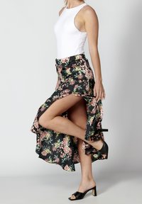 Kukkakuvioinen maksihame, jossa on musta pohja, pinkkejä ja vihreitä kuvioita, korkea halkio ja röyhelöt helmassa. Yhdistetty mustiin korkokenkäsandaaleihin.