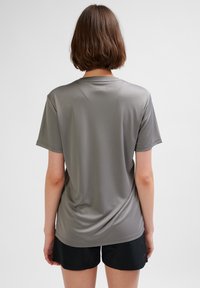 Szara koszulka z krótkim rękawem wykonana z gładkiego, lekkiego materiału. Charakteryzuje się luźnym krojem i okrągłym dekoltem, zestawiona z czarnymi szortami.