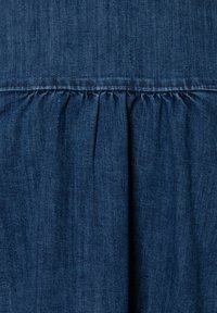 Blue denim fabric with gathered pleats below a horizontal seam, showing texture and stitching details.