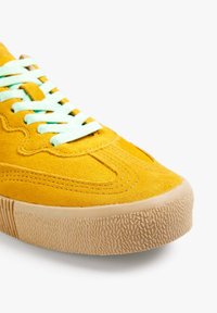 Sneaker giallo in suede con lacci verde menta, suola in gomma testurizzata, design affusolato e cuciture decorative nell'area della punta.