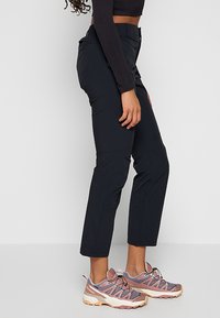 Czarne, dopasowane spodnie z gładk�ą fakturą i czterema kieszeniami, zestawione z jasnoróżowymi i szarymi butami do wędrówek o solidnej podeszwie.