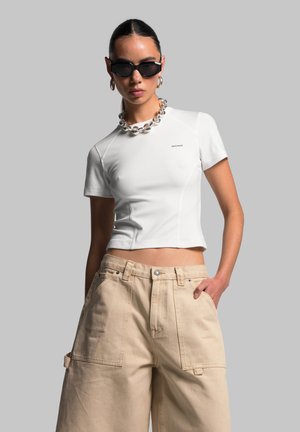 White cropped t-shirt with raglan sleeves, smooth texture, and small branding. Paired with beige wide-leg cargo pants featuring pockets.